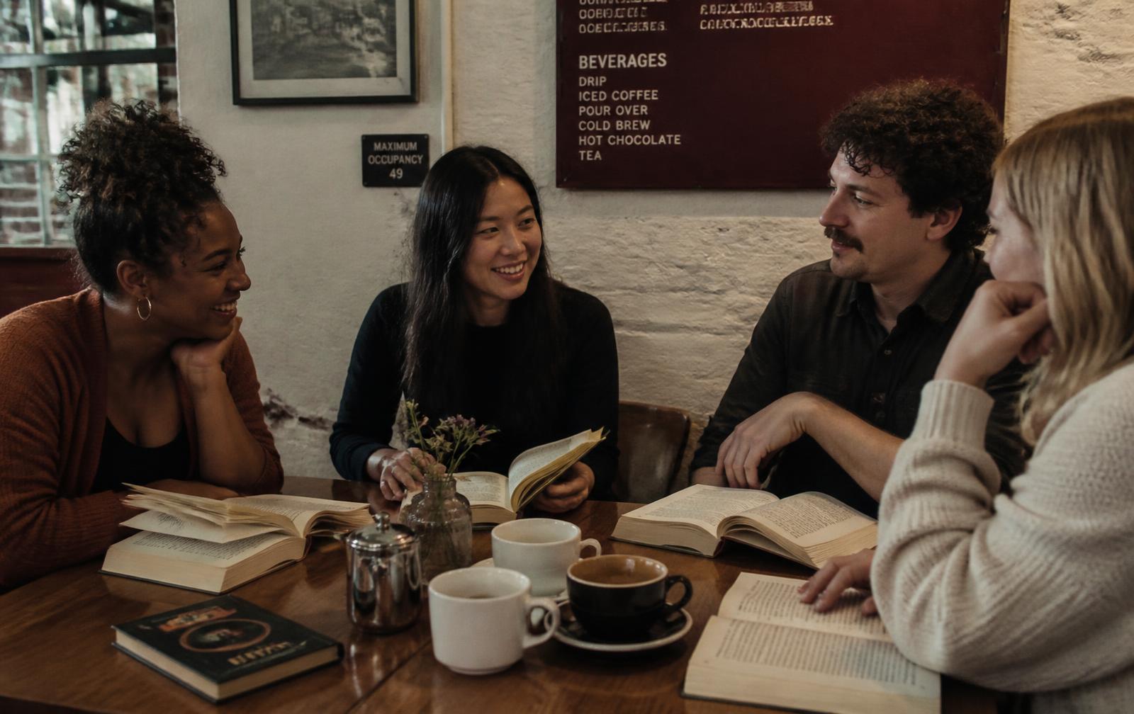 Four readers talking around a cafe table with open books and coffee cups